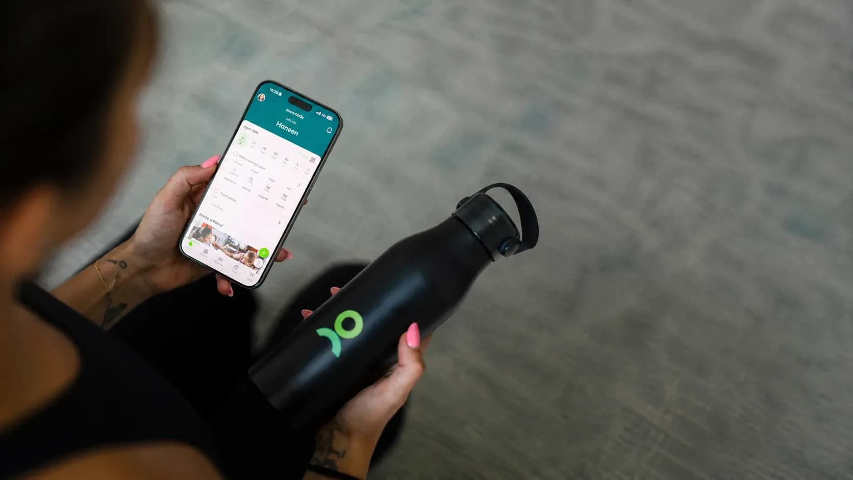 Person tracking fitness and stress levels on a mobile app with smartwatch and water bottle