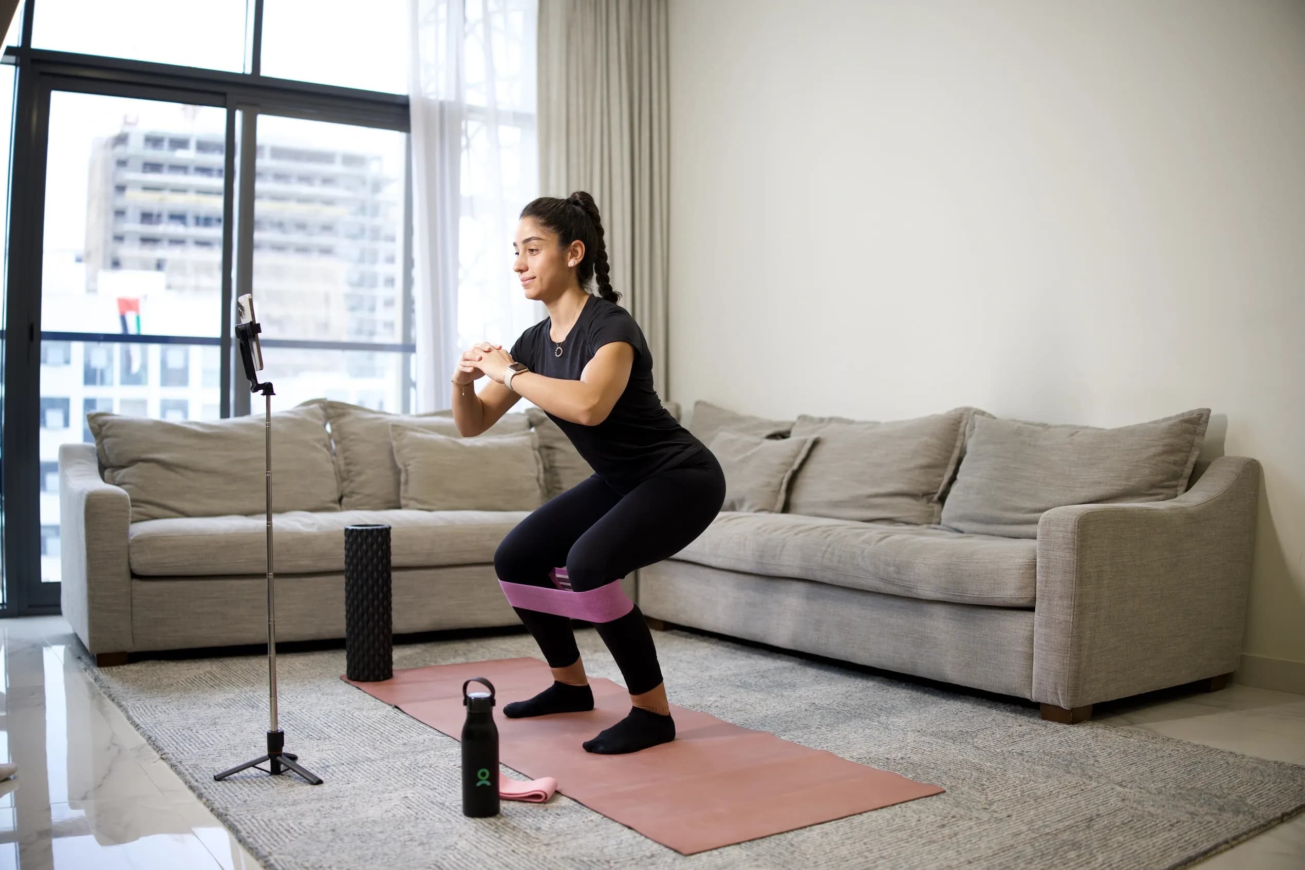 every mom fitness coaching program woman training at home with resistance band following everybody coach on phone in Dubai