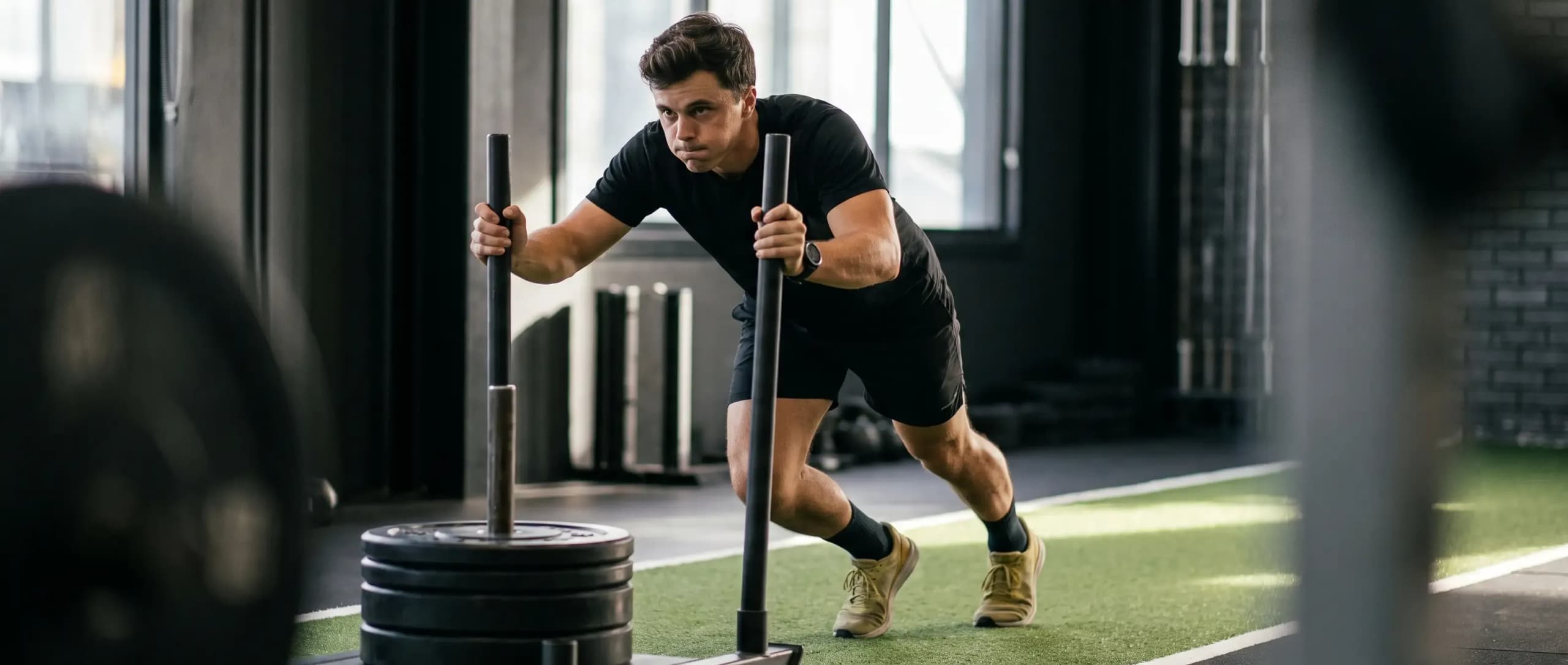 Athlete pushing a weighted sled during HYROX training in a gym